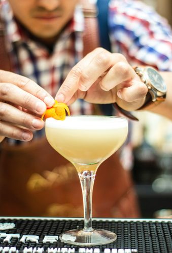 Bartender garnishing a cocktail with a citrus twist