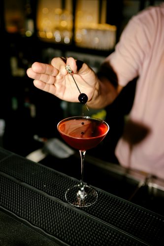 Bartender dropping a cherry garnish into a cocktail