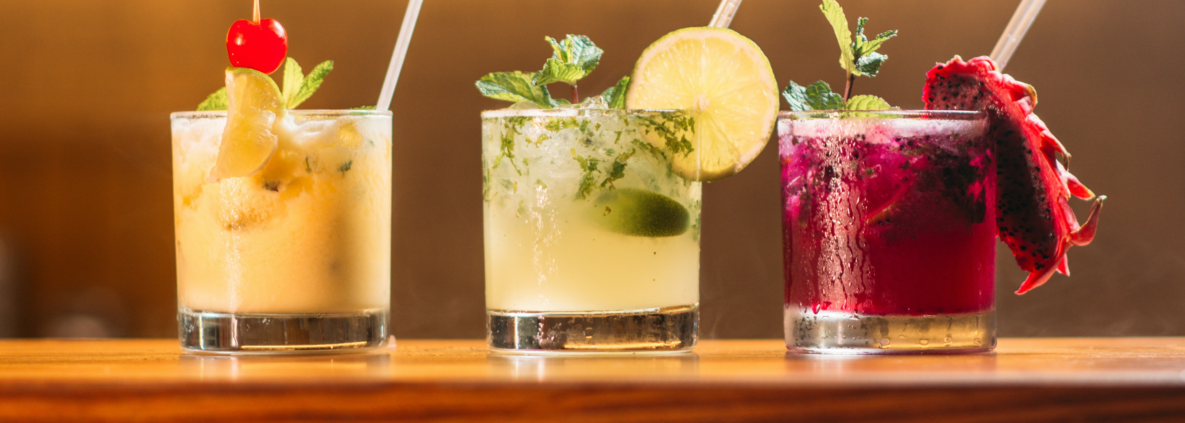 Three colorful craft cocktails on a bar